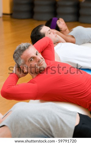 Healthy people with mature instructor doing sit-ups on fitness ball at gym