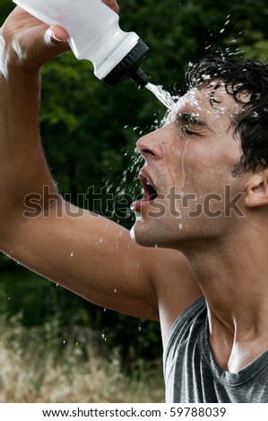Young tired athlete splashing and pouring fresh water on his head to refresh during a running trail
