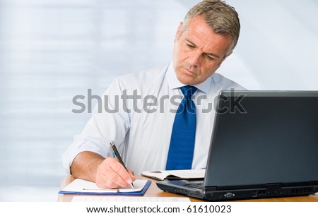 Absorbed mature businessman working and taking notes in his modern office