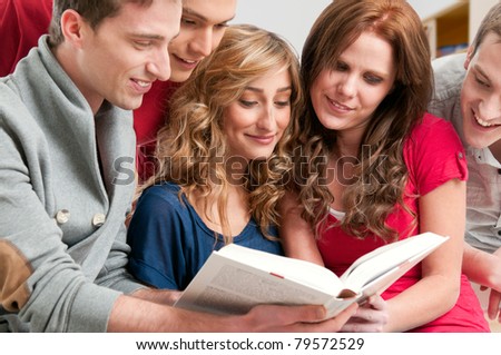 Happy young college students studying together on a textbook in a library