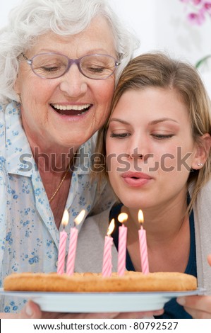 Happy smiling grandmother celebrating and giving a birthday cake to her grandson at home