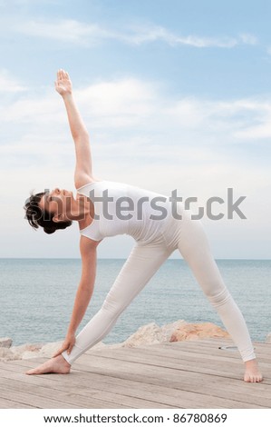 Healthy young woman practise yoga outdoor at sea: trikonasana pose