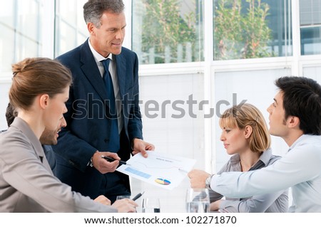 Mature manager discussing with his worker colleagues about paperwork in office