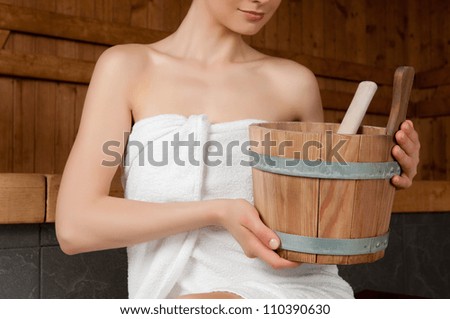 Beautiful young lady holding a bucket in a sauna