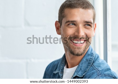 Confident young man looking away with big smile. Happy handsome guy looking through window thinking about the future. Closeup face of smiling casual man imagine with copy space.