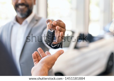 Closeup hand of cardealer giving new car key to customer. Salesman hand giving keys to a client at showroom. Man's hand receiving car keys from african agent in a auto dealership with copy space. Foto stock © 