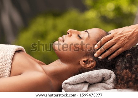 Beautiful black woman getting face massage in luxury spa. African american girl relaxing in resort spa while getting head massage. Masseuse hands massaging black woman with closed eyes at resort spa.