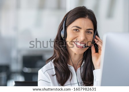 Call center agent with headset working on support hotline in modern office with copy space. Portrait of mature positive agent in conversation with customer over headset looking at camera.