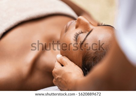Beautiful african woman getting face massage in beauty spa. Black girl with closed eyes relaxing in outdoor spa while getting head massage. Serene woman relaxing outdoor in a beauty center.