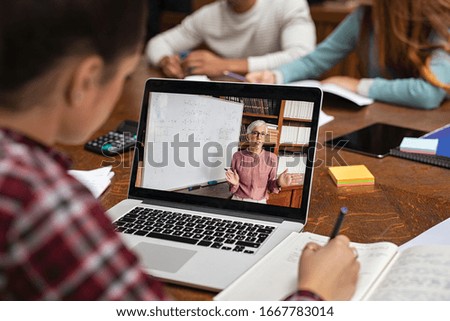 Teacher explaining lesson in video call while girl taking notes. Rear view of university student understanding concepts online while making notes. Young woman studying on computer and writing on notes