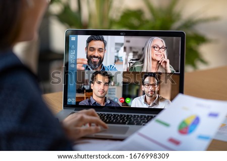 Photo of Back view of business woman talking to her colleagues about plan in video conference. Multiethnic business team using laptop for a online meeting in video call. Group of people smart working from home