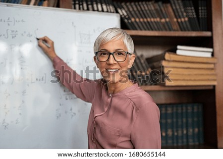 Portrait of happy mature professor teaching mathematics to students in a library. Senior smiling woman solving math problem while writing on white board. Portrait of tutor looking at camera. Photo stock © 