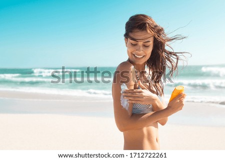 Beautiful young latin woman applying suntan lotion at sea with copy space. Tanned girl in bikini applying sunscreen on shoulder at tropical beach. Woman protecting skin with sunblock cream from UV.