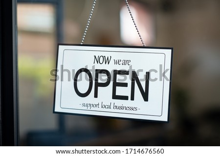 Reopening of a small business activity after the covid-19 emergency, ended the lockdown and quarantine. A business sign that says now we are open support local businesses hang on door at entrance.