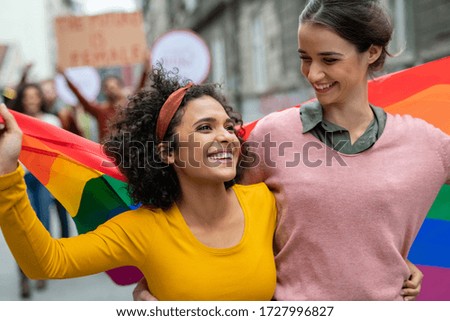 Young women on street enjoying holding gay pride flag during protest. Smiling multiethnic women enjoying during march on street for lgbt rights. Diversity, tolerance and gender identity concept. Сток-фото © 