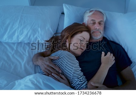 Senior man and woman sleeping and dreaming together in a deep sleep. Mature woman embracing and sleeps on her husband's chest while sleeping at night. Loving couple resting in their bed, copy space. Stock fotó © 