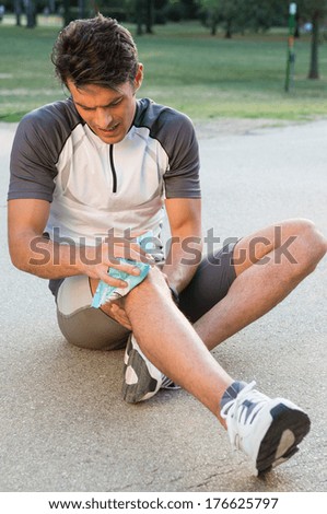 Young Male Athlete Sitting On Ground And Taking Ice For Knee Pain