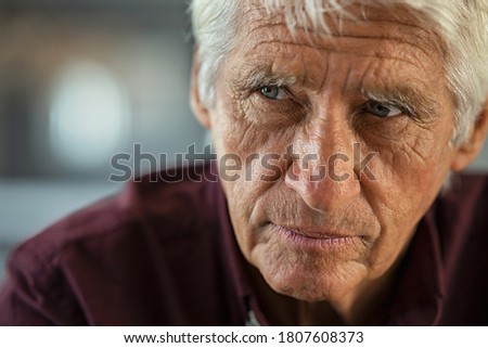 Thoughtful senior man sitting on couch looking away with copy space. Depressed sad man thinking at home. Elderly pensive senior suffering from alzheimer disease.