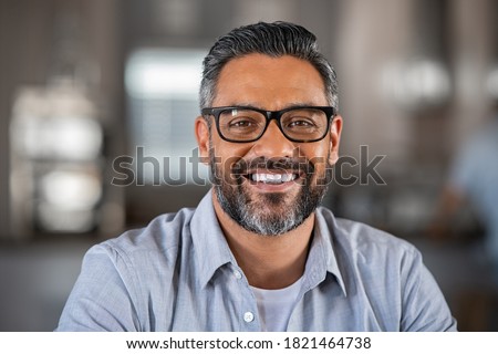Smiling mature indian man wearing spectacles and looking at camera. Middle eastern confident businessman at office. Portrait of successful mid entrepreneur feeling satisfied and working from home.