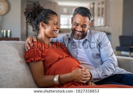 Mid adult couple expecting a baby while husband caresses the belly of his pregnant african woman. Lovely indian man touching belly of his girlfriend and feeling baby movement.