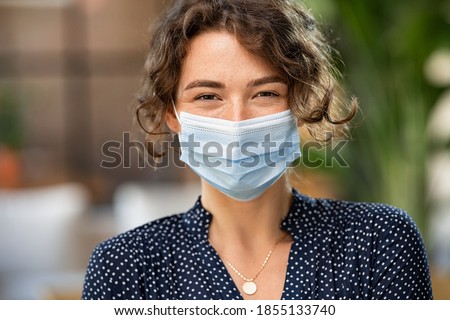 Portrait of happy young woman wearing face medical mask. Hopeful girl with protective face mask looking at camera. Smiling woman wearing safety protective mask to fight against covid-19 pandemic.