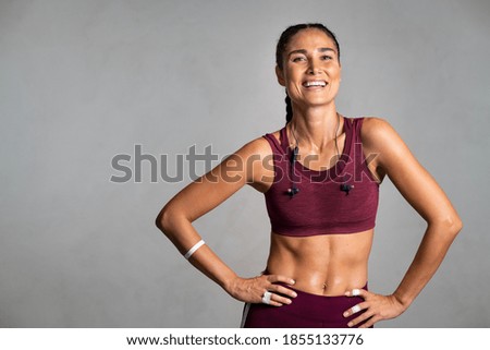 Portrait of beautiful fitness woman smiling and looking at camera isolated on grey background. Mid woman in sportswear relaxing after training at gym. Happy fit girl on gray wall with copy space.