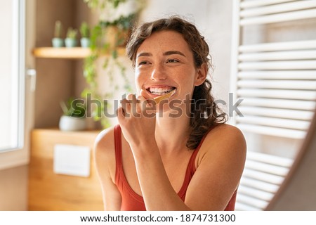 Smiling young woman brushing teeth in bathroom. Happy girl looking in mirror while using ecological toothbrush with whitening toothpaste. Beauty girl in bathroom cleaning teeth in the morning time.