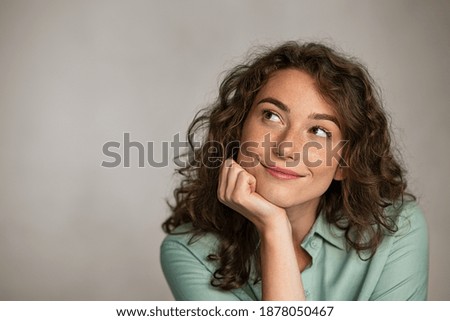 Portrait of young thoughtful woman with hand on chin having an idea against grey background. Pensive woman looking away while thinking. Close up face of girl planning her future isolated on gray wall.