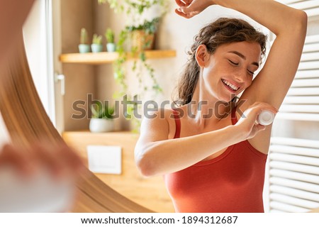Beautiful young woman using deodorant under armpit in bathroom during morning time. Girl applying deodorant roll on after shower on underarms. Girl using antiperspirant roll-on at home after waking up