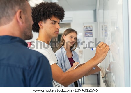 Young african man solving mathematics problem. College student solving algebra equation on white board in classroom. High school black guy trying to understand mathematics problem during lesson.