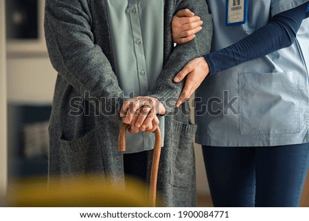 Close up hands of caregiver doctor helping old woman at clinic. Nurse holding a senior patient with walking stick. Elder woman using walking cane at nursing home with nurse holding hand for support. 