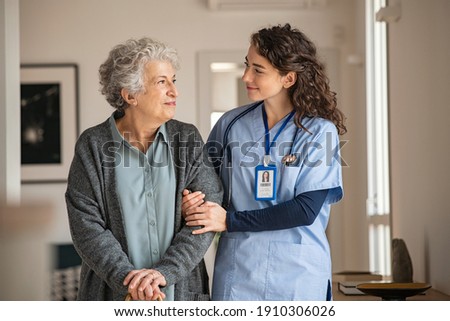 Young caregiver helping senior woman walking. Nurse assisting her old woman patient at nursing home. Senior woman with walking stick being helped by nurse at home. 商業照片 © 