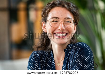 Portrait of laughing young woman wearing spectacles in office. Carefree casual girl wearing glasses and looking away. Confident beautiful student wearing specs and smiling.