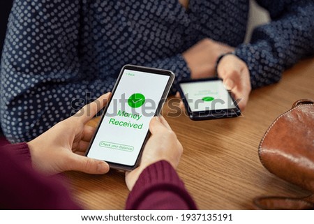 Close up of woman hands holding mobile phone with application to receive money. People holding smart phone and making cashless payment transaction. Smartphone screen displaying money received message.