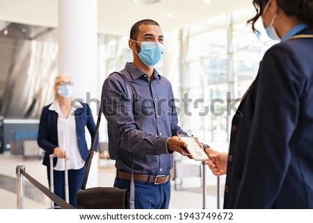 Indian passenger wearing protective face mask showing e-ticket to flight attendant at boarding gate. Mixed race businessman showing boarding pass on mobile phone to air hostess during covid pandemic.