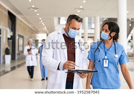 General practitioner and nurse wearing surgical face mask against covid-19 while having a discussion in hospital hallway. Worried doctor showing medical report to nurse wearing protective face mask.