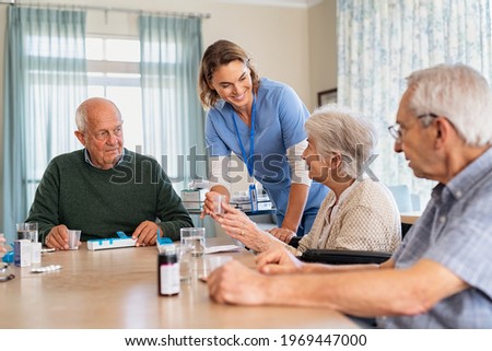 Nurse giving medicine to group of seniors at retirement community. Happy smiling nurse gives medicines to elderly patients at nursing home. Happy senior woman taking her dose of medicines.