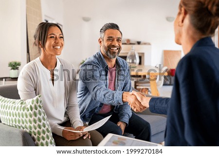 Mature indian man shaking hands with financial advisor at home. Happy smiling couple greeting broker with handshake at home. Multiethnic mid adult man and hispanic woman sealing a contract.