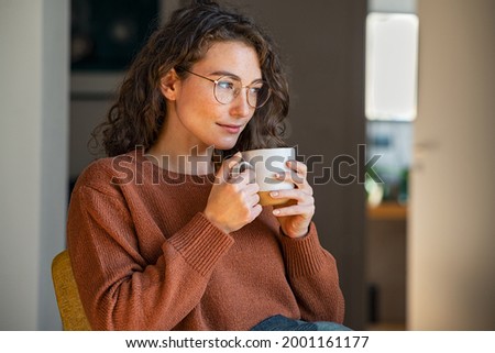Pensive woman drinking hot coffee at home. Thoughtful young woman drinking a cup of tea while thinking. Pretty contemplative girl with sweater relaxing at home while drinking purifying herbal tea. Foto d'archivio © 