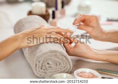 Close up shot of a woman in a nail salon receiving manicure by beautician with metal nail file. Woman getting nail manicure at spa centre. Beautician file nails to a customer in luxury salon.  Foto d'archivio © 