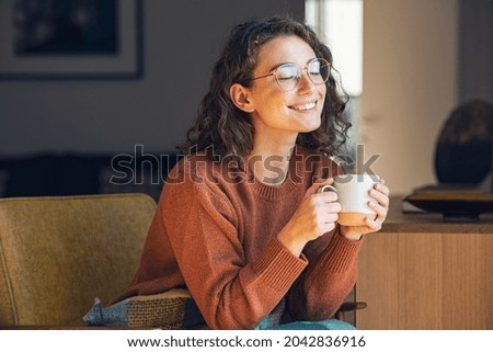 Happy young woman drinking a cup of tea in an autumn morning. Dreaming girl sitting in living room with cup of hot coffee enjoying under blanket with closed eyes. Pretty woman wearing sweater at home. Сток-фото © 