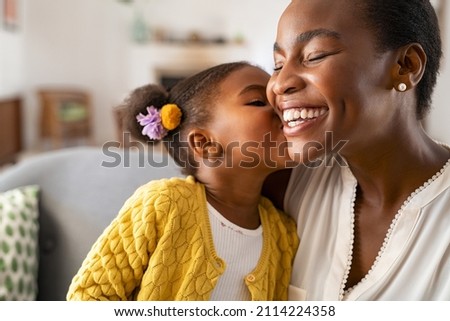 Photo of Close up of beautiful daughter kissing mother on cheek at home. African little girl giving kiss to happy mother. Lovely black female child kissing cheerful and proud woman on cheek for mother's day.