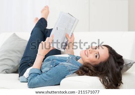 Smiling Happy Woman Lying On Sofa Reading A Magazine