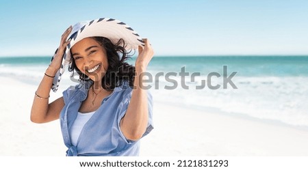 Photo of Portrait of stylish latin hispanic woman with white straw hat standing at beach. Young smiling woman on vacation enjoy sea breeze wearing straw hat and looking at camera. Attractive beautiful girl.