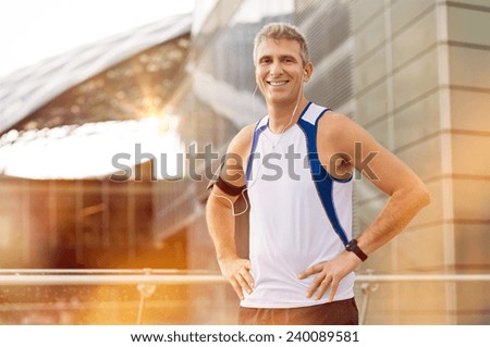 Portrait Of Happy Mature Male Jogger With Earphone Looking At Camera Outdoor