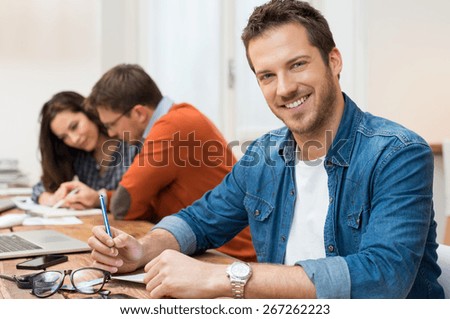 Portrait young business man looking at camera with workers sitting in background in office