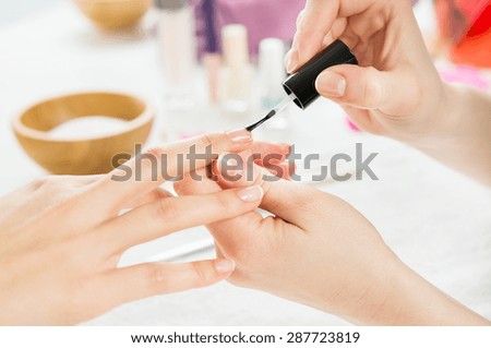 Closeup shot of a beautician applying nail polish to female nails. Woman getting nail manicure. Shallow depth of field with focus on nail polish.