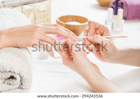 Closeup shot of a woman using a cuticle pusher to give a nail manicure. Nail technician giving customer a manicure at nail salon. Young caucasian woman receiving a french manicure.