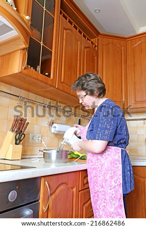 A woman housewife prepares food using a mixer in the kitchen