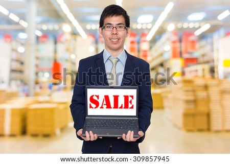 Businessman holding digital laptop computer showing word of  sale, superstore background
